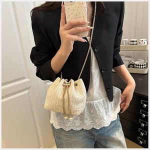 Close-up of woven straw bucket bag featuring gold chain strap and pearl drawstring detail