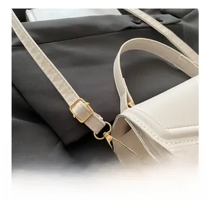 Close-up of adjustable shoulder strap with gold metal buckle on a cream crossbody bag