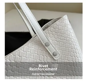 Close-up of white woven leather tote bag featuring durable silver rivet reinforcement
