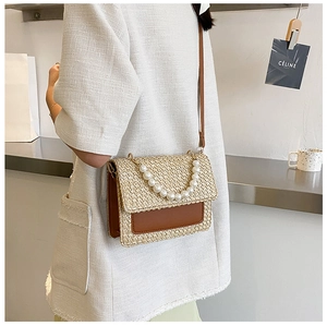 Detail of woven straw handbag featuring pearl top handle and brown leather shoulder strap