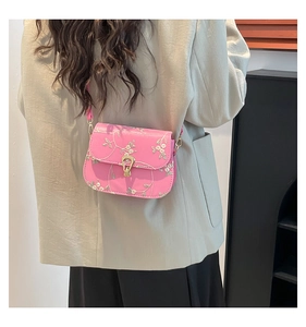 Detail of pink faux leather saddle bag with white and green floral embroidery on it