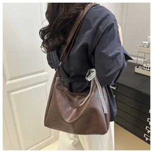 Detail of a brown leather shoulder bag featuring a decorative white lace-up side tie