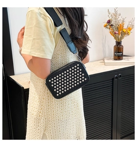 Detail of a black square camera bag with silver rivets and wide nylon shoulder strap