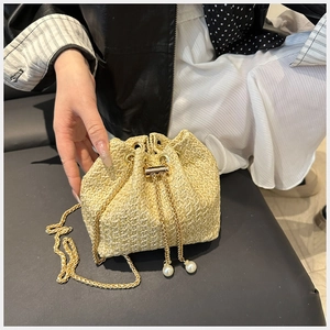 Close-up of beige woven bucket bag with gold chain strap and elegant pearl drawstrings