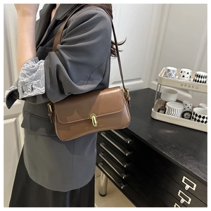 Brown leather underarm bag with a golden metal buckle shown in a modern interior setting