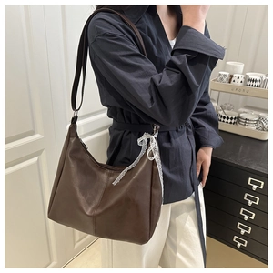 Detail of dark brown leather hobo bag featuring a white lace bow and adjustable strap