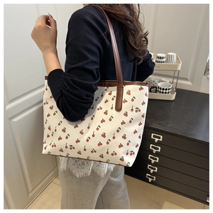 Détail d'un grand sac cabas beige avec imprimés cerises et anses en cuir marron foncé
