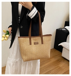 Détail d'un sac cabas en paille tissée avec lanières en cuir marron et étiquette logo
