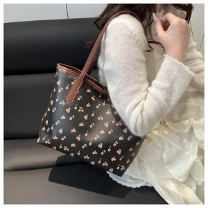 Detail of a black leather tote bag featuring cherry print and brown shoulder straps