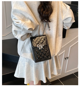 Chic quilted black phone bag with silver bow buckle worn on a shoulder chain