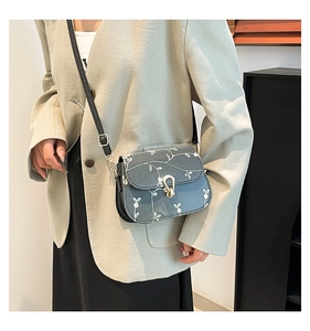Vue détaillée de la broderie florale et du fermoir en fer à cheval doré sur un sac bandoulière