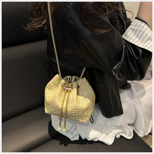 Detail of woven straw bucket bag featuring a drawstring closure and pearl chain strap