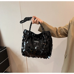 Detail of a black sequin tote bag with a fashion logo label and woven handle texture