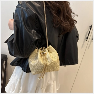 Detail of straw bucket bag with gold chain strap and pearl drawstring tassels on model