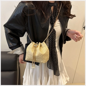 Detail of straw bucket bag with gold chain strap and pearl accents on black leather jacket