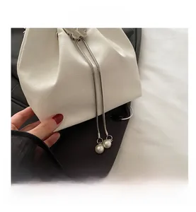 Close-up of white croc-embossed bucket bag with silver bow buckle and pearl pendant detail