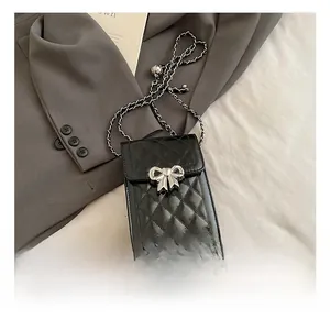 Detail of black quilted phone bag with silver bow buckle and woven metal chain strap