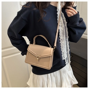 Detail of light khaki flap handbag featuring round gold buckle and smooth leather texture