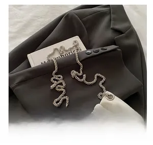 Detailed view of white crocodile texture bucket bag with heavy silver chain on grey suit