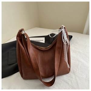 Close-up of brown textured leather shoulder bag with delicate white lace ribbon detail