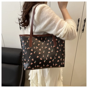 Detailed view of cherry print tote bag with brown straps worn on a person's shoulder