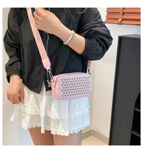 Pink mini crossbody bag with metal rivets and wide shoulder strap shown on a model