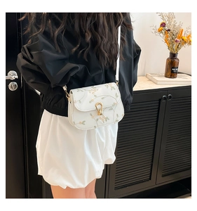 Detail of floral embroidery and gold metal clasp on white leather crossbody square bag