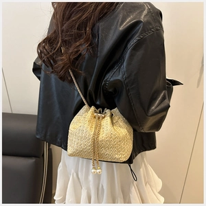 Detailed shot of beige straw bucket bag featuring a gold chain and faux pearl drawstring charm