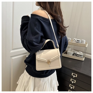 Detail of cream leather crossbody bag with golden twist lock on model in casual outfit