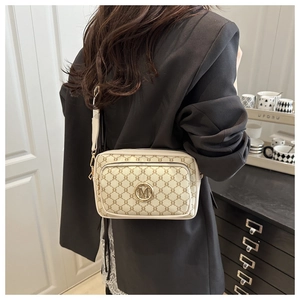 Detail view of cream vintage crossbody bag with letter print and metal M logo on model