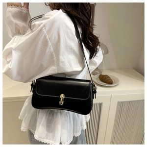 Detail of a black minimalist baguette bag featuring a gold U-shaped metal buckle and strap