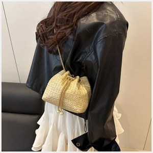 Detail of beige woven bucket bag with gold chain strap and elegant pearl drawstrings