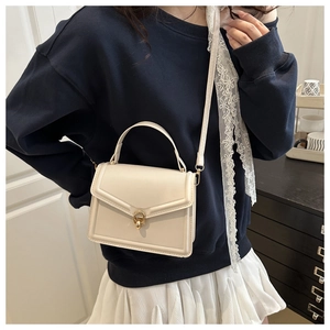 Petit sac carré blanc cassé avec boucle métallique et bandoulière porté par un mannequin