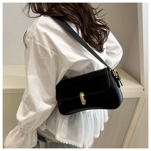 Detail of a black rectangular leather underarm bag with a vintage gold oval metal clasp
