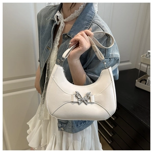 Détail d'un sac hobo blanc avec boucle papillon argentée porté par un mannequin en extérieur
