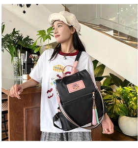 Detail of black nylon backpack featuring pink handles and colorful plush pom-pom charms