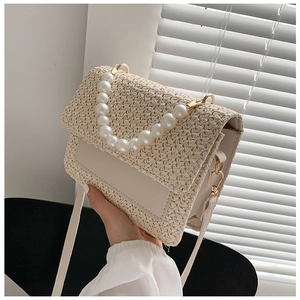 Detail of woven cream handbag featuring decorative pearl handle and leather crossbody strap