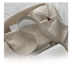 Close-up of white leather bag with gold rotating lock on a beige blazer and book