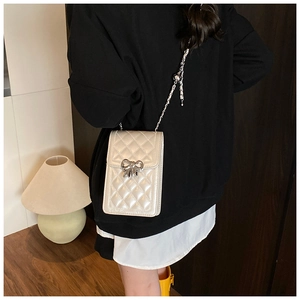 Close-up of white quilted mini crossbody bag featuring a silver bow and metal chain strap