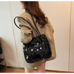 Detail of black sequined tote bag with woven strap and fashion brand label shown on model