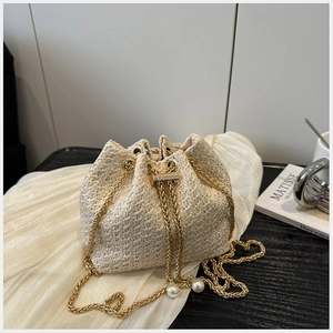 Detail of straw woven bucket bag with pearl drawstring and gold chain strap