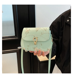 Detail of mint green saddle bag featuring floral lace embroidery and golden horseshoe buckle