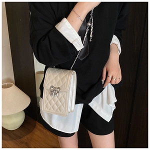 Detail of quilted crossbody phone bag with metal bow clasp and chain strap on model