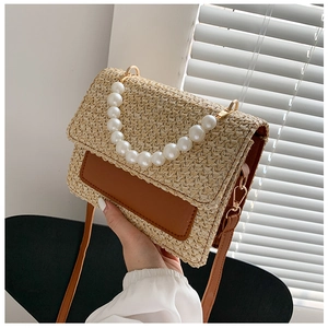 Detail of straw woven handbag featuring oversized pearl handle and brown leather flap