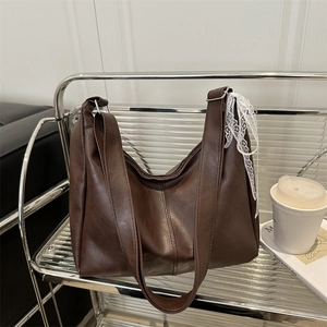 Brown soft leather tote bag with lace ribbon and silver buckle on minimalist metal shelf