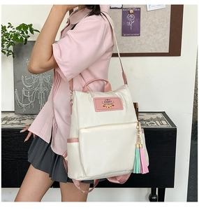 Detail of cream nylon backpack featuring pink bunny logo and mint green tassel accessory