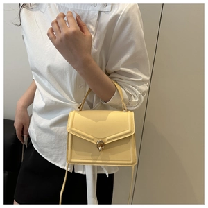 Detail of cream yellow leather satchel featuring a golden twist-lock clasp and flap design
