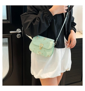 Detail of mint green saddle bag featuring delicate floral embroidery and metal buckle
