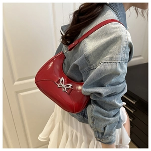 Gros plan d'un sac à bandoulière en cuir verni rouge avec un fermoir papillon argenté