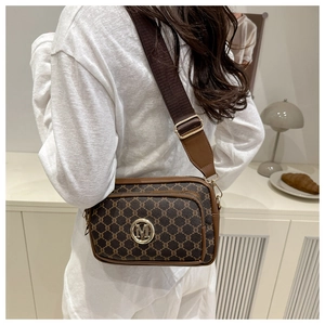 Close-up of brown monogram crossbody bag with gold M-logo and wide fabric strap